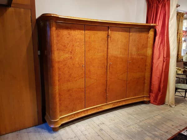 A fabulous Swiss four door wardrobe with burr walnut veneer exterior and sumptuous satin wood veneer interior. The front of the wardrobe is a gentle inward curve between two columns in an Egyptian deco style with central decorated column carved at top and bottom.